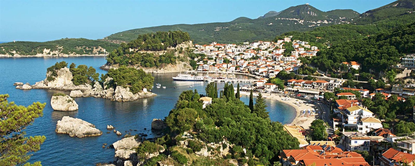 Parga seen from above: white and orange houses around the harbour, the castle headland and the Panagia islet in a blue bay