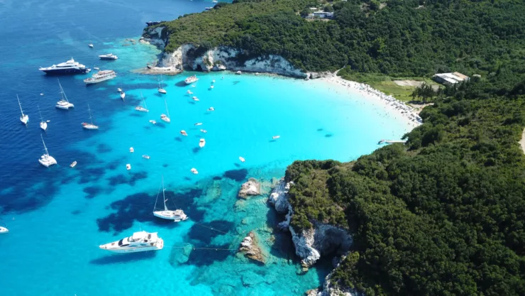 A bright turquoise bay with yachts and sailing boats beside a wooded coast